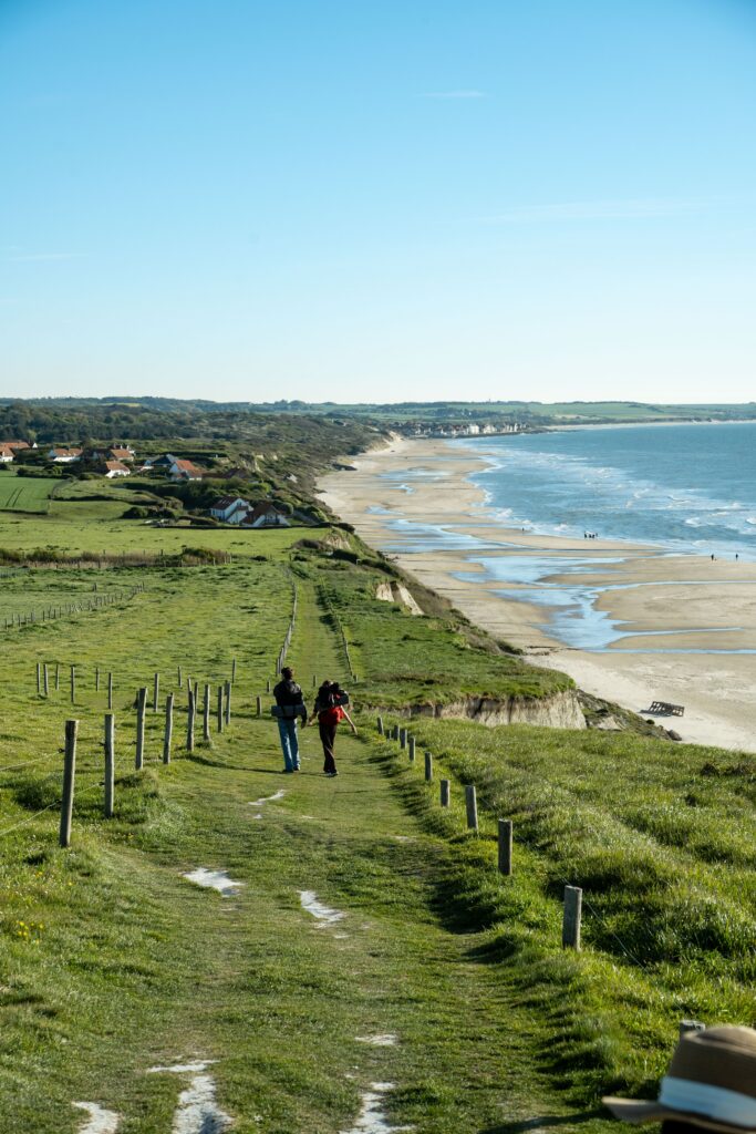 Two people walking on a beautiful coastal path in Escalles, France, under a clear blue sky.